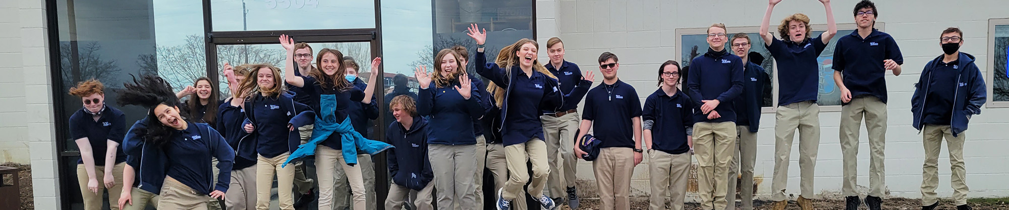 Group of high school students waving to the camera in front of a building