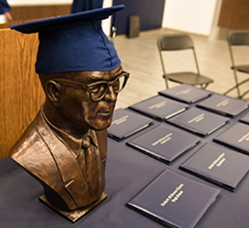 A man's bust next to diplomas on a table